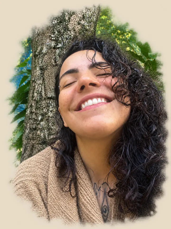 Mulher sorrindo de olhos fechados, ao sol, encostada no tronco de uma árvore