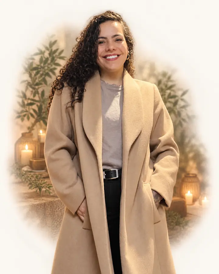 Mayara Rocha sorrindo, de casaco bege, em um ambiente aconchegante com plantas e velas